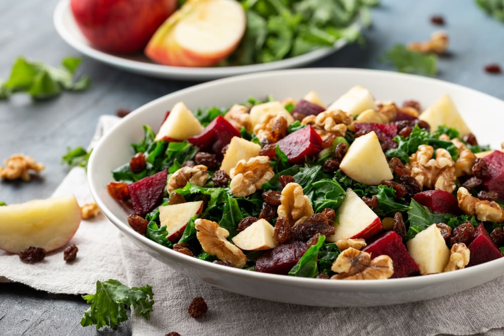 Kale salad with apple, beetroot, walnut and raisins in white plate — healthy anti-inflammatory meal